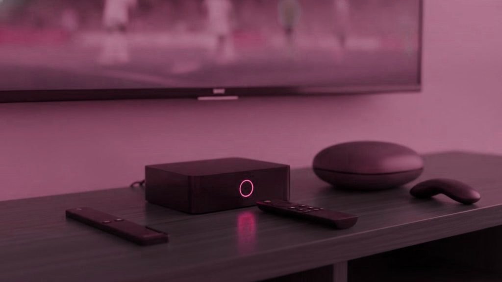 Three IPTV devices, a streaming stick, a set-top box and a round streaming puck, with their remotes on a TV console
