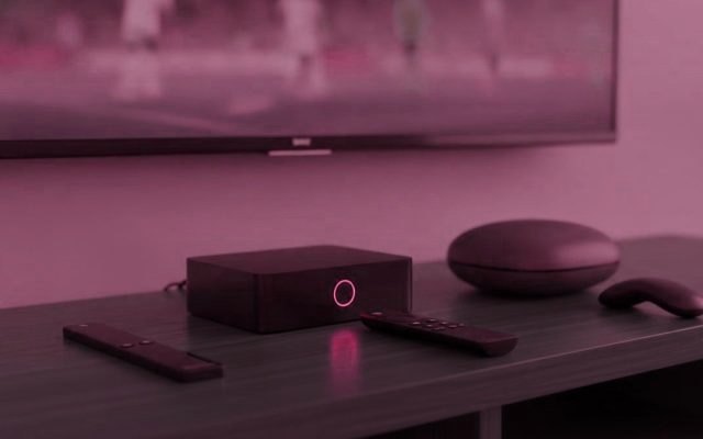 Three IPTV devices, a streaming stick, a set-top box and a round streaming puck, with their remotes on a TV console