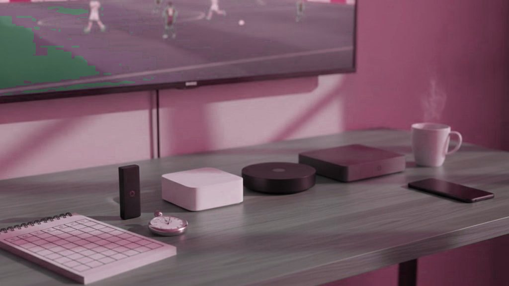 Five streaming devices beside a scoring notepad and a stopwatch, in front of a TV showing a soccer match