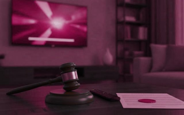 A gavel, a streaming remote and a sealed legal document on a coffee table before a switched-on television